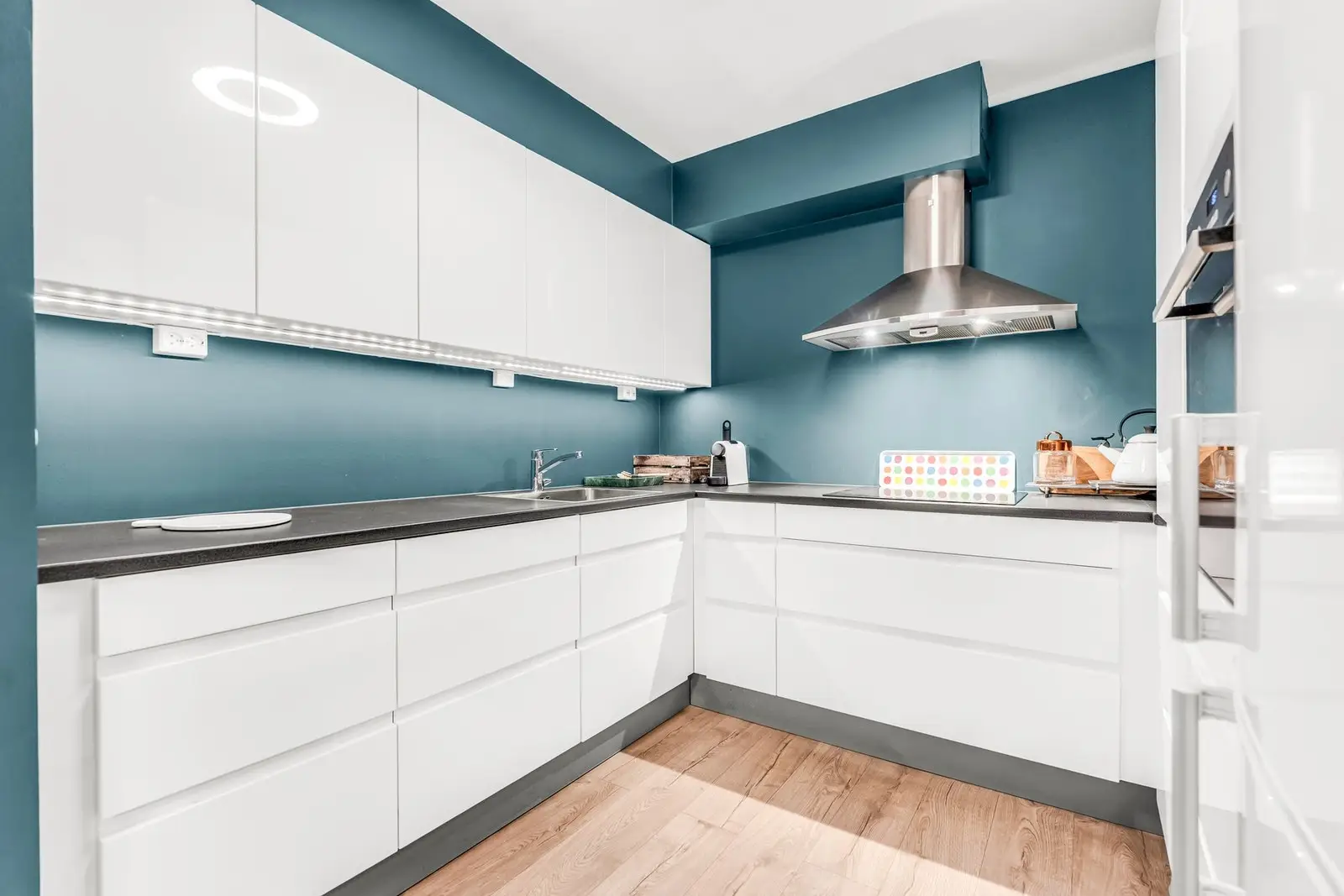 Moderne kjøkken med hvite skapfronter, blå vegger og innebygd ventilator.